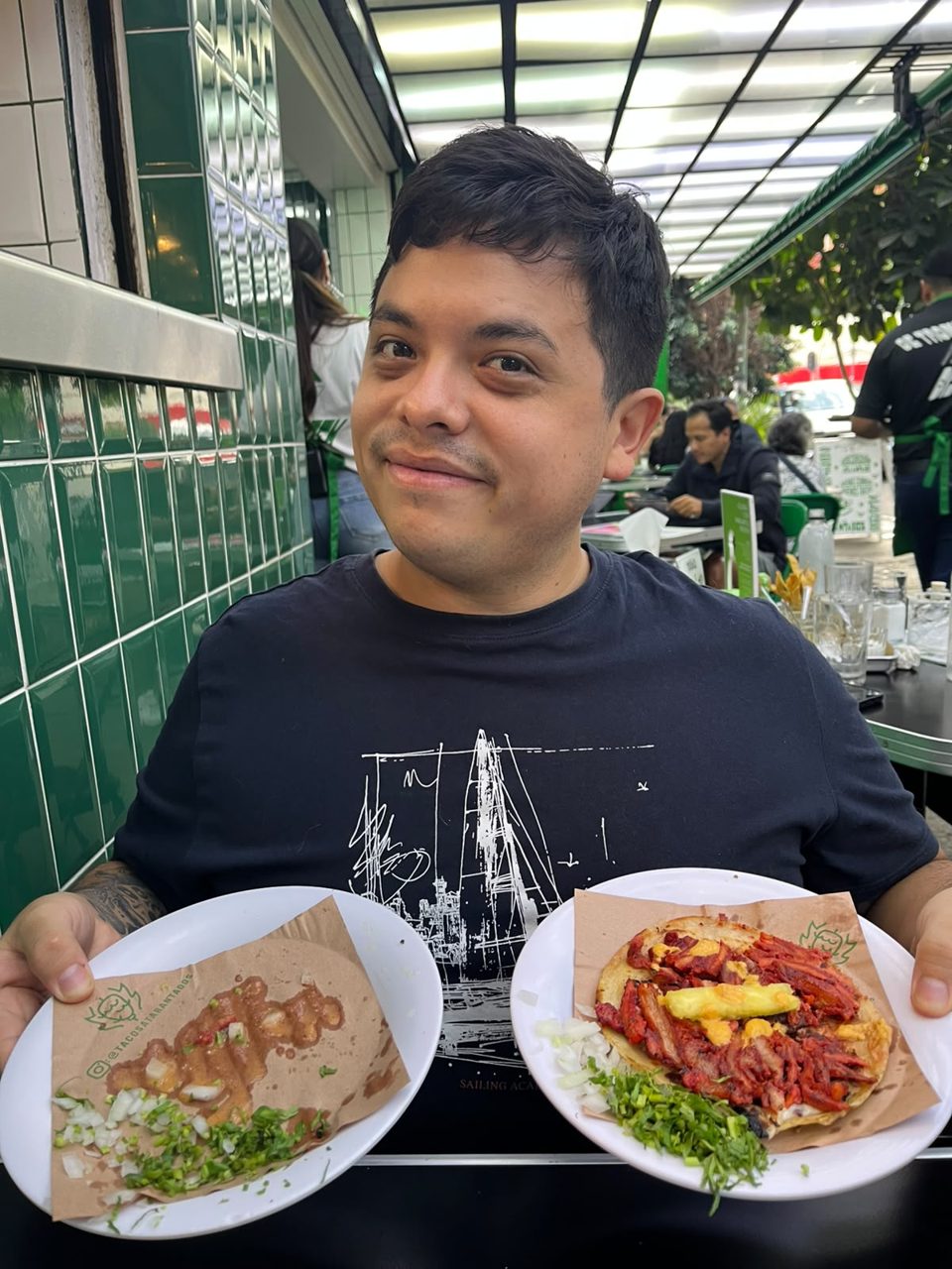 José G. sosteniendo un plato de tacos de trompo negro y una cachetada en Tacos Atarantados, Roma Norte, CDMX