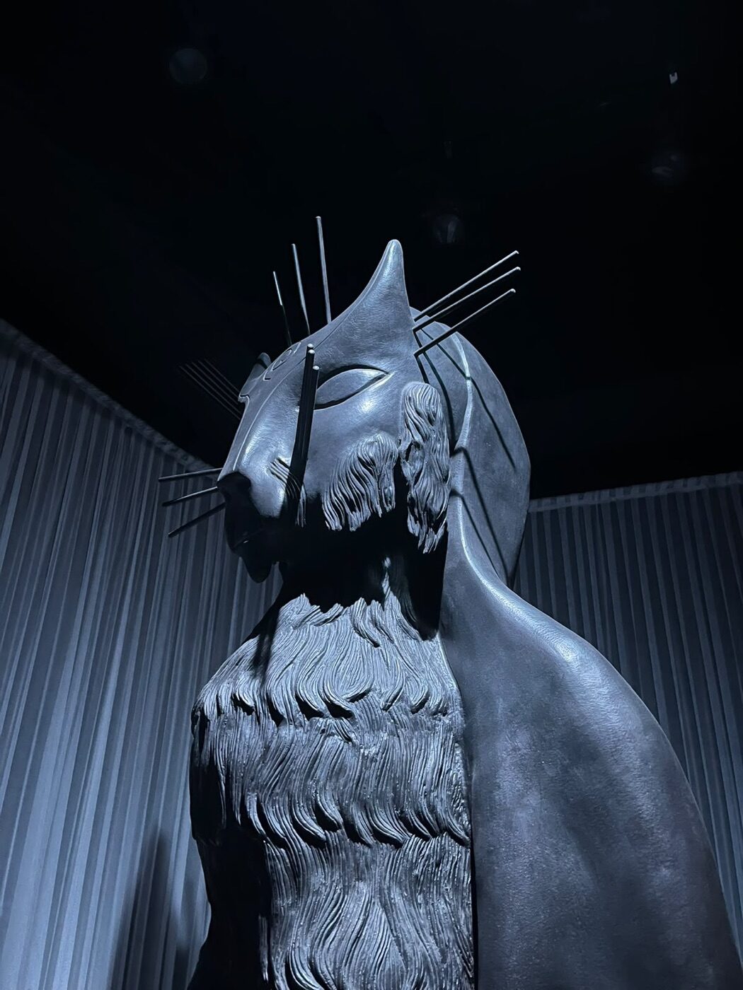 Escultura monumental de figura felina con bigotes metálicos y melena tallada, de Leonora Carrington, vista desde abajo