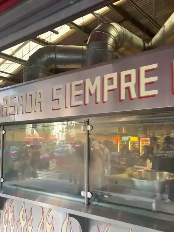 Ventanal de Asaderos Orozco con el letrero Carne asada siempre lista y la parrilla detrás del vidrio
