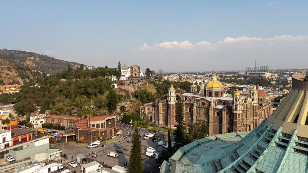 Vista aérea del recinto de la Basílica de Guadalupe con la nueva basílica de techo de cobre, la antigua basílica de cúpulas amarillas y el cerro del Tepeyac al fondo