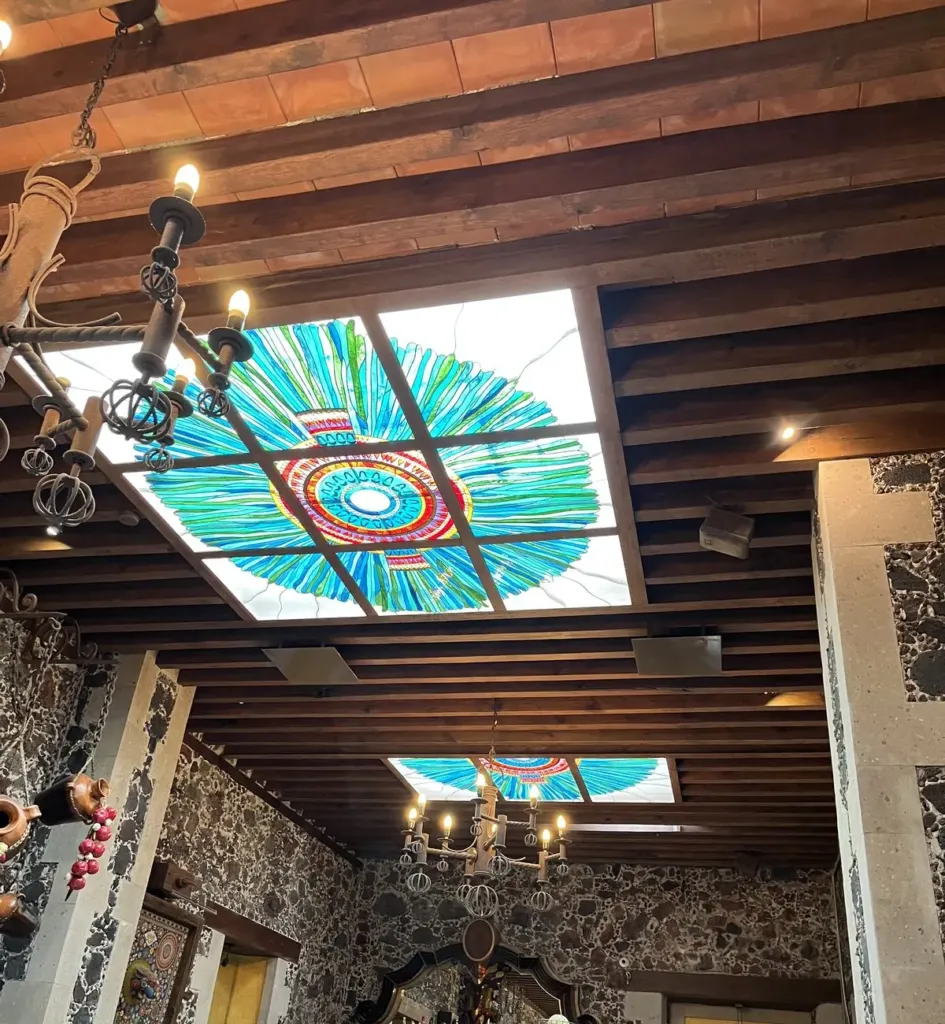 Techo de vigas de madera de Café de Tacuba con dos vitrales en forma de penacho, candiles de hierro forjado y la barra al fondo