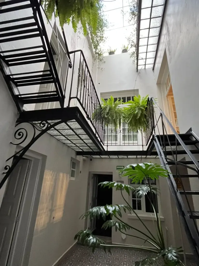 Patio interior de Casa Goliana con escaleras de hierro negro, plantas colgantes y tragaluz