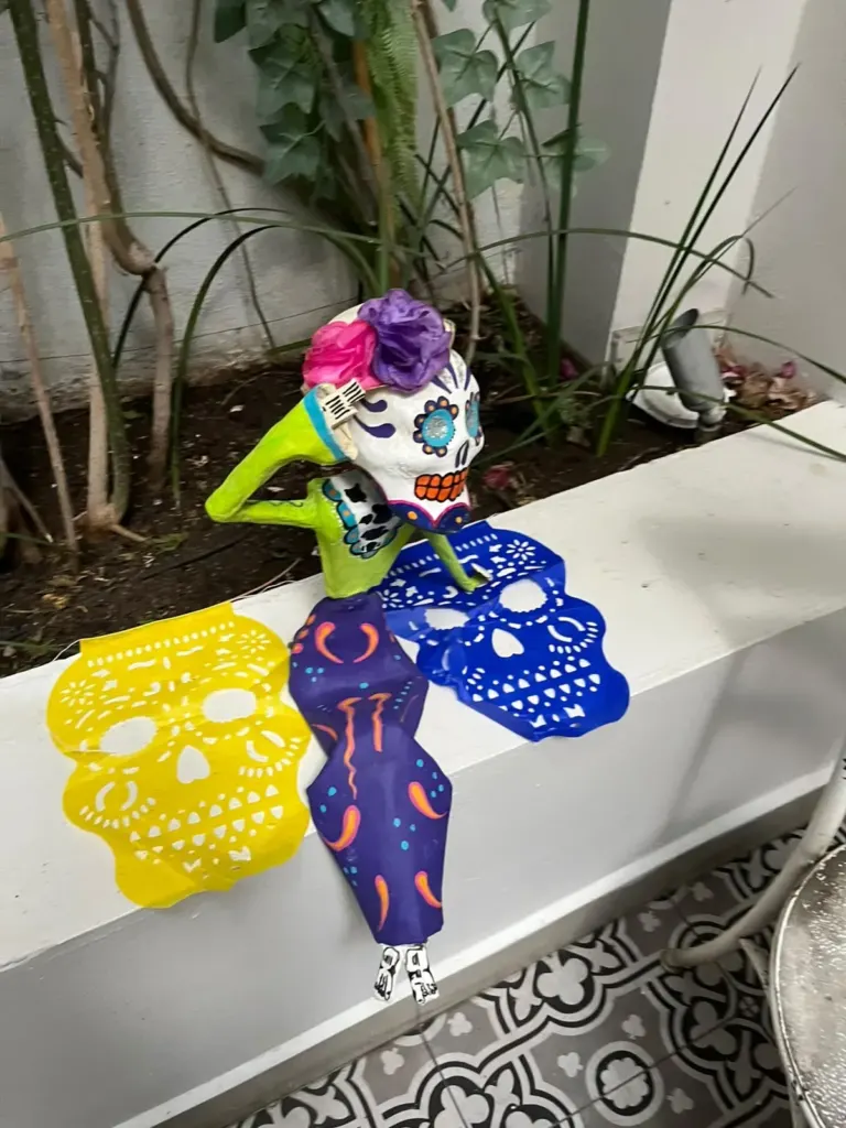 Calaveras de papel con flores y papel picado amarillo y azul decorando una jardinera del patio de Casa Goliana