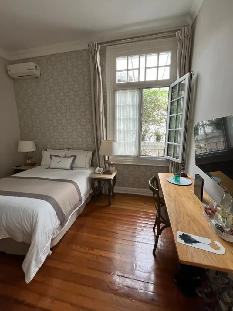 Habitación de Casa Goliana con cama blanca, pisos de duela, escritorio de madera y ventana a la calle