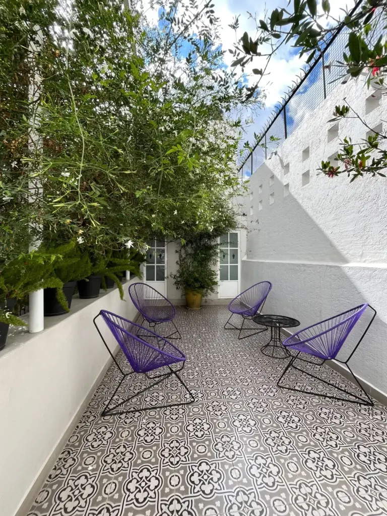 Terraza de Casa Goliana con sillas acapulco moradas, plantas y piso de mosaico