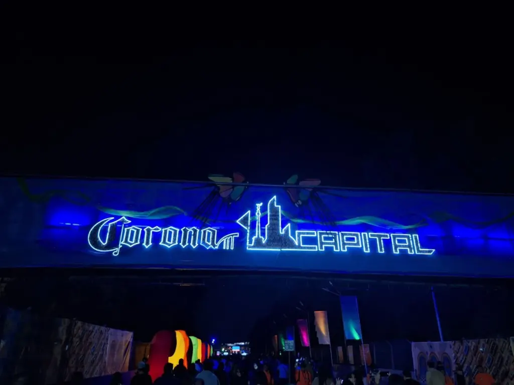 Arco de entrada iluminado en azul con el letrero de Corona Capital de noche, con asistentes entrando al festival