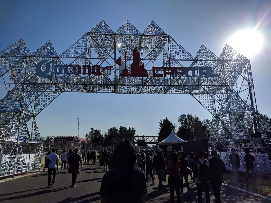 Gente caminando bajo el arco metálico de entrada del Corona Capital en el Autódromo Hermanos Rodríguez, de día