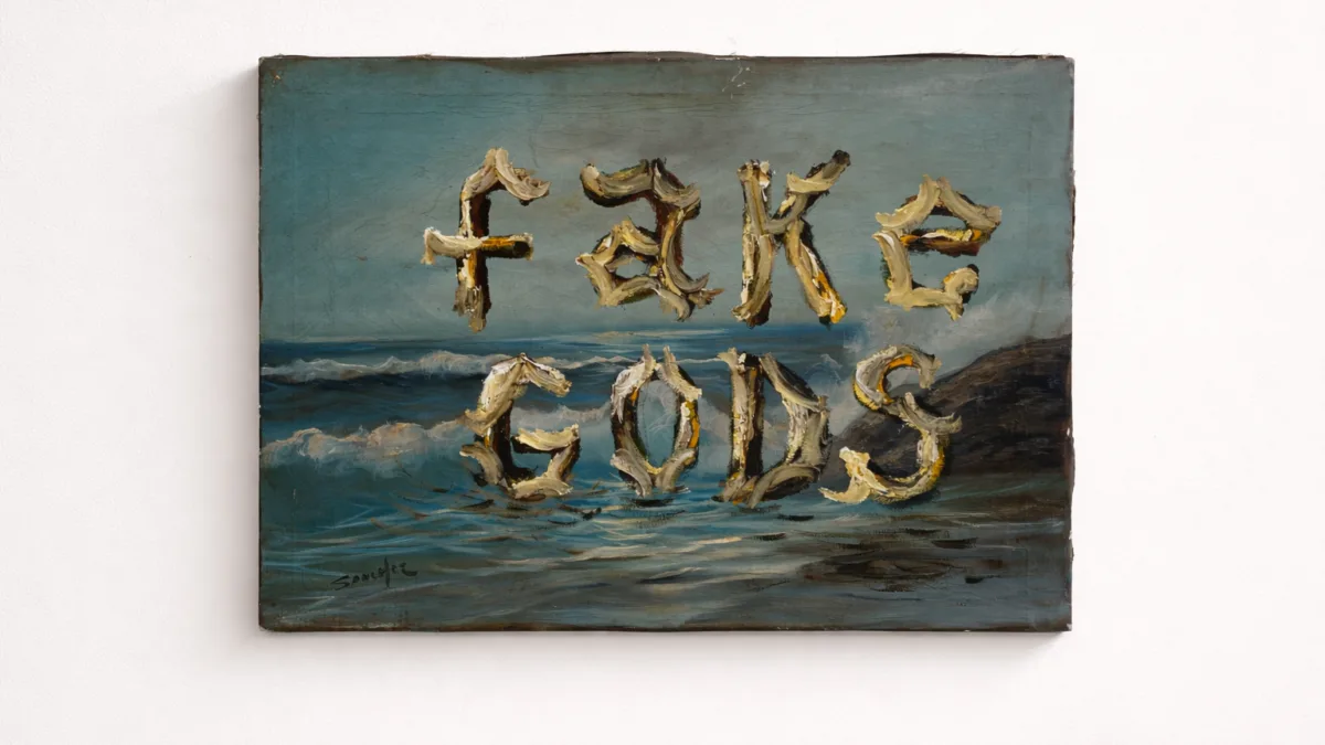 Pintura al óleo de un mar con las palabras «FAKE GODS» formadas con letras de aspecto óseo, colgada en una pared blanca