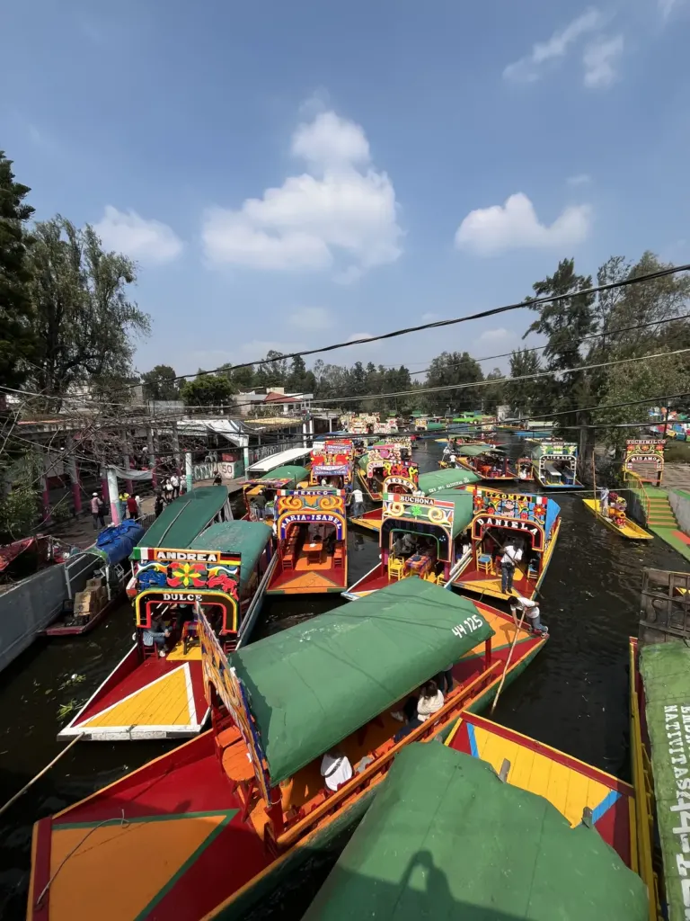 Trajineras de colores con nombres pintados en sus arcos, amarradas en el embarcadero Nuevo Nativitas de Xochimilco
