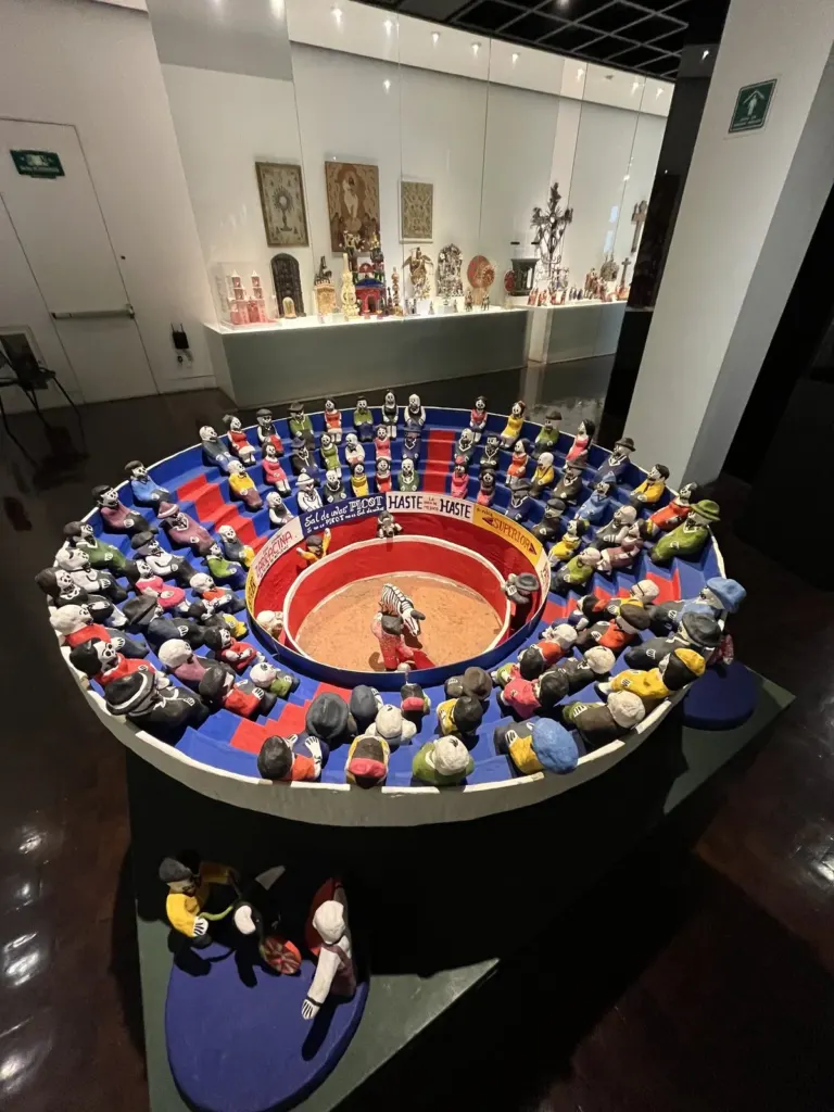 Sala del Museo de Arte Popular con la plaza de toros de calaveras al frente y una vitrina al fondo con piezas de arte popular