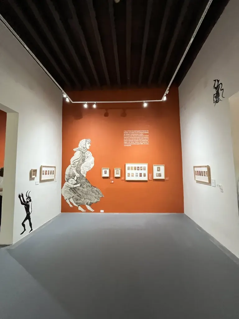 Sala del Museo Nacional de la Estampa con un muro naranja, una figura de mujer grabada en gran formato y estampas enmarcadas en fila