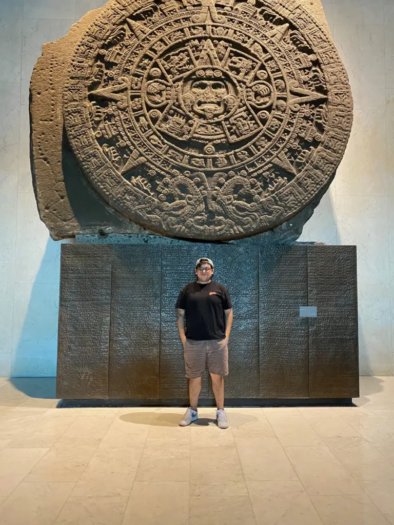 Piedra del Sol en su muro de la sala mexica del Museo Nacional de Antropología, con un visitante de pie debajo, mayo de 2024
