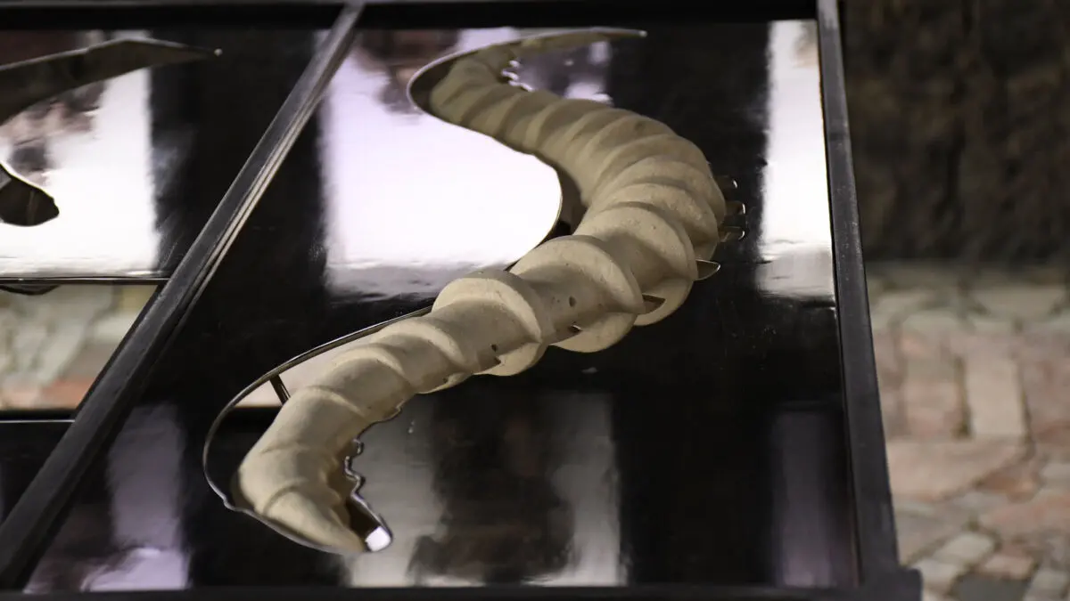 Escultura de bronce con forma de cola o columna vertebral sobre una estructura metálica negra en River Rouge, de Yeni Mao