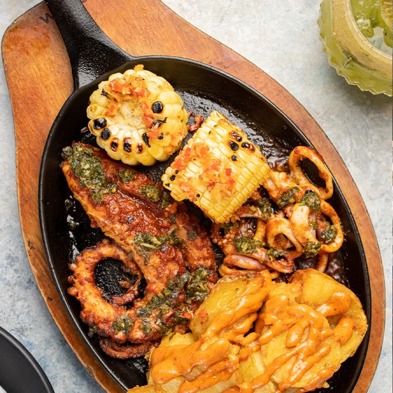 Pulpo a la parrilla con choclo y papas en sartén de hierro en Yakumanka